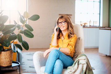 Smiling mature woman sitting in the armchair and having a phone call