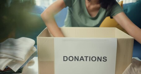 Happy young Asia teenage girl volunteer packing clothes product into donation cardboard boxes while working in charitable foundation. Social worker, coronavirus and quarantine concept. Closeup shot.