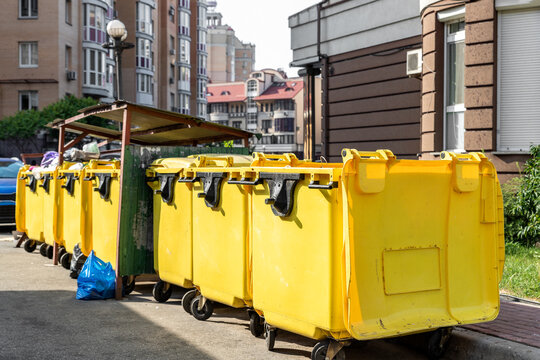 Rows of many big plastic yellow dumpster cans full of black plastic trash litter bags near residential building at city downtown or suburban area. Non-recyclable sorting garbage collecting