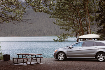 lakeside campsite with picnic table fire pit ring and campvan, raining day cloudy, green jade color...