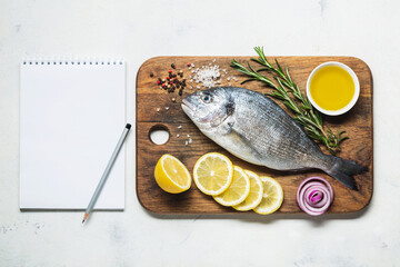 Dorado fish on a rustic wooden cutting board with spices and a notebook for recipe or menu.