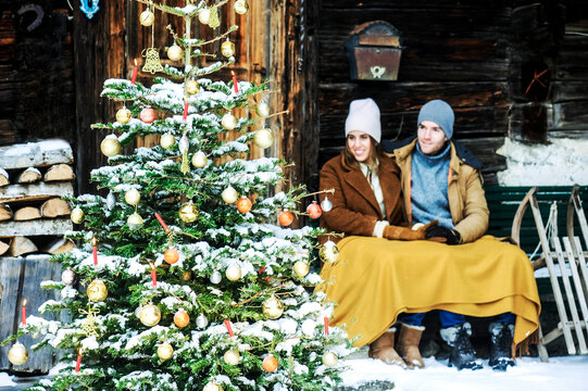 Smiling couple looking at Christmas tree while sitting in front of farmhouse