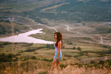 Naklejka premium Beautiful slender woman on top of a mountain at sunset. Amazing landscape with a gradient of mountains. The concept of sports and active life.
