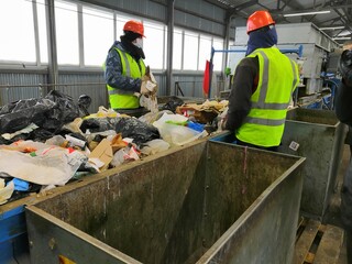 male migrant workers in green vests and orange helmets are sorting household garbage on the automatic tape of the garbage landfill