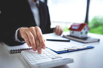 A young woman's hand presses a calculator to determine and summarize the cost of mortgage home loans for refinancing plans, lifestyle concepts.