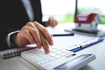 A young woman's hand presses a calculator to determine and summarize the cost of mortgage home loans for refinancing plans, lifestyle concepts.