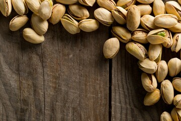 Border of salted, roasted green pistachio nuts snack on wood background, healthy food snack, copy space