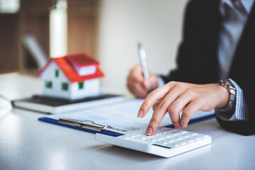 A young woman's hand presses a calculator to determine and summarize the cost of mortgage home...