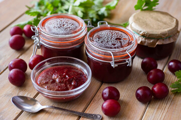 Preservation for the winter: spicy tkemali sauce from cherry plums in jars on a wooden table. Close-up