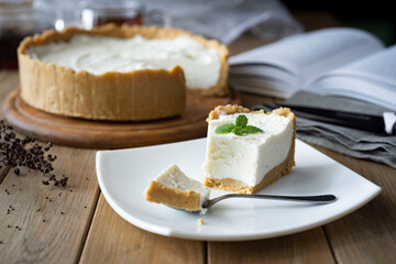 Sweet dessert for breakfast: a piece of cheesecake on a white plate and a cheesecake in the background. Close-up