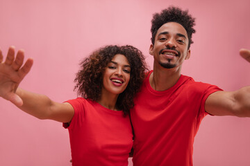 Portrait of hispanic happy, young couple taking selfie on pink background. High-quality photo of guy and girl, looks fashionable and happy. Emotions and states of mind, concept