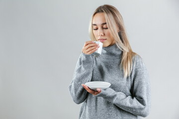 woman wearing warm sweater drinks a hot tea on grey background, studio shot. the concept of warming up with a hot drink. 