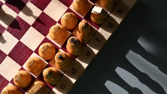 Camera sliding over chess figures on white side with dark shadows. Overhead view of chess board game with white pieces