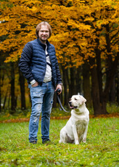 Man looks at camera while having a walk with retriver dog. Fabulous autumn park in golden colors. Full body portrait. Closeup