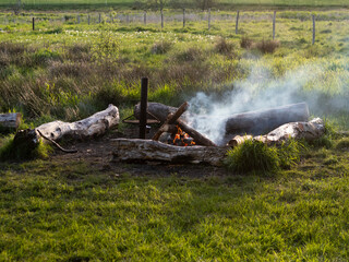 Campfire with logs and smoke at a campsite in field area with green grass.