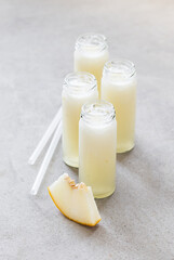 Summer refreshing melon cocktail drink in tall glass bottles with straws on a light gray background