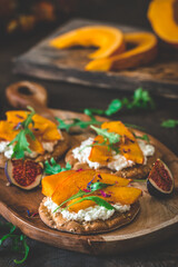 Round crispbread slices with grainy cream cheese, roasted pumpkin and rocket salad on wooden background, vertical