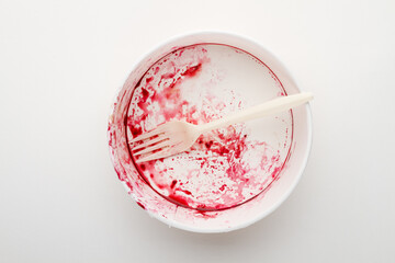 Dirty disposable bowl and fork after eating on a white background