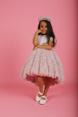 a small dark-skinned beautiful girl in a lush pink dress with a crown on her head