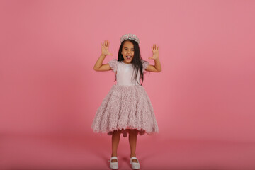 a small dark-skinned beautiful girl in a lush pink dress with a crown on her head