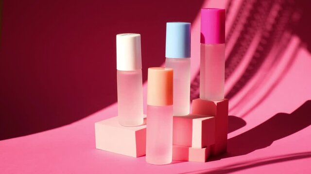 shade from a swaying palm leaf on several spray glass bottles with perfume on pink geometric podiums