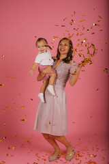 
a young mother in a pink dress holds her little son in her arms for a confetti party