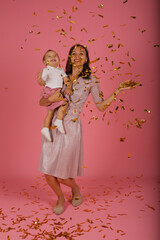 
a young mother in a pink dress holds her little son in her arms for a confetti party