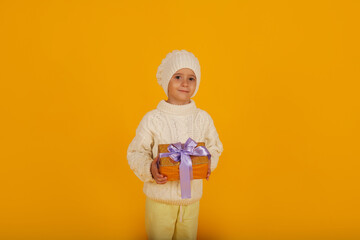 a boy in a white winter hat in a knitted white sweater holds a gift box in his hands