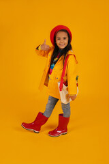 a girl in a red beret with pink glasses in a yellow raincoat and red boots has a bag with autumn flowers on her shoulder