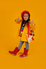 a girl in a red beret with pink glasses in a yellow raincoat and red boots has a bag with autumn flowers on her shoulder