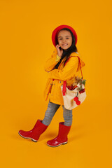 a girl in a red beret with pink glasses in a yellow raincoat and red boots has a bag with autumn flowers on her shoulder