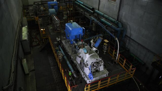 Engineers in helmets check new powerful compressor on ground in contemporary production plant workshop upper view