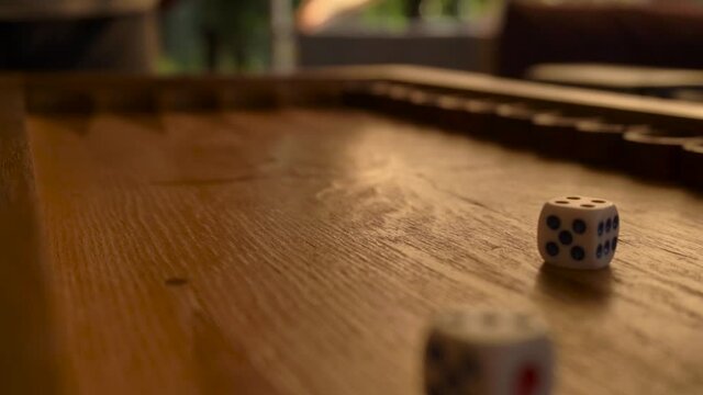 a man's hand throws colorful dice on a wooden backgammon board