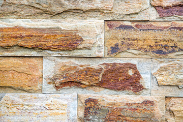 The background of the wall is made of rectangular tiles of natural stone, the bark of a tree is gray, beige and brick color with a beautiful stone pattern. Backgrounds texture design.