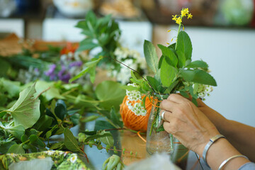 woman's hands putting together a flower arrangement on table surrounded by plants
