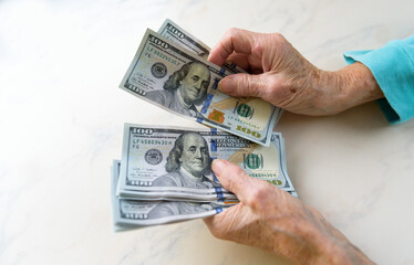 Close-up of an elderly woman's hands holding money in 100 dollar bills