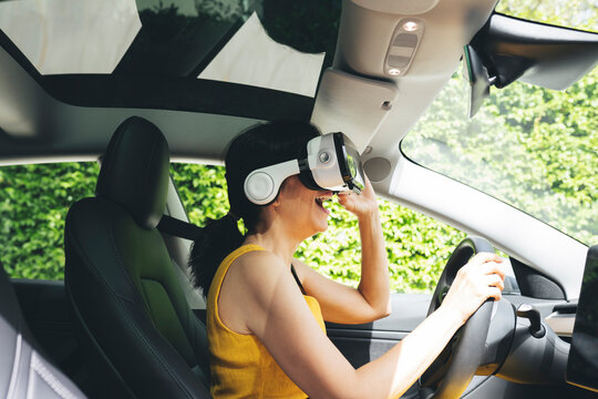 Excited woman wearing virtual reality simulator while driving electric car