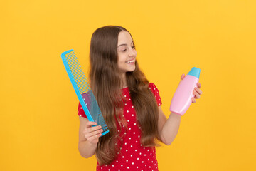 happy kid combing long hair. hairdresser. girl has wavy hairdo hold hairbrush