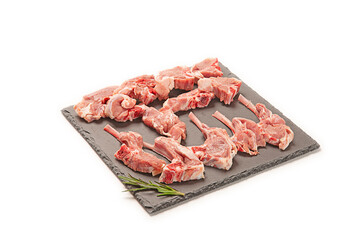 chuletas de cordero frescas crudo cortadas sobre una pizarra negra con hojas de romero decorativo. aislada fondo blanco