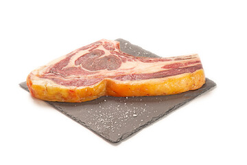 chuletón de buey fresco crudo y sal gorda decorativa sobre un plato de pizarra negro. aislada fondo blanco