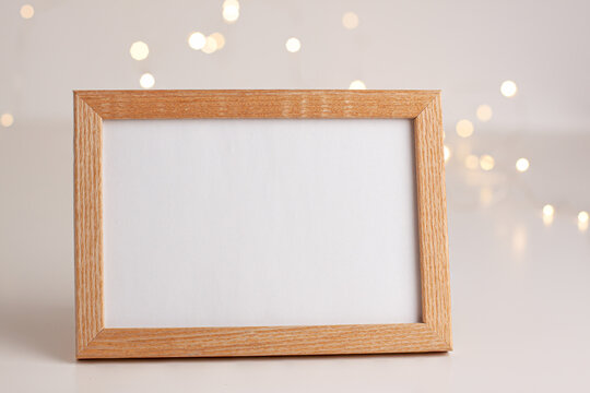 Close Up Of Horizontal Mockup White Canvas Paper Frame For Photography With Wooden Borders On Bright Background With Gold Bokeh. Product Advertising Concept With Copy Space