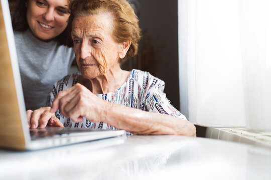 Smiling young woman assisting grandmother using laptop at home
