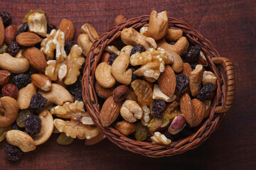 basket with dried fruits (pistachio, raisins, almonds, peanuts, walnuts) on wooden board (from avobe view)