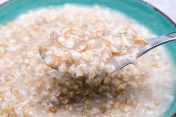 A spoon of cooked oats porridge above a green bowl, healthy breakfast and dieting product close up, tasty vegan food