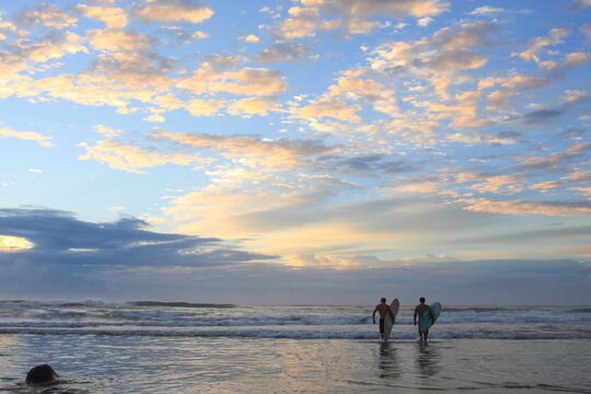two surfers walking on the beach to the ocean at sunrise