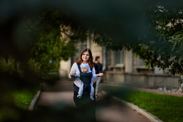 Young mother with infant in baby sling walk outdoors.