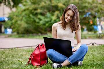 Young woman sits in park with laptop during online learning.