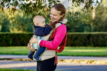 Happy young mother with baby in sling outdoors.