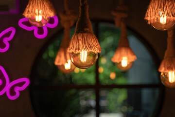 Vintage ceiling chandelier incandescent light bulbs from hemp rope with pink neon butterfly interior, round window, and green nature background.