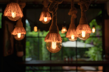 Vintage ceiling chandelier incandescent light bulbs from hemp rope with pink neon butterfly interior, round window, and green nature background.